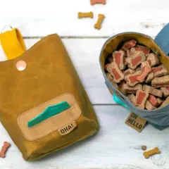 Deux sacs à friandises pour chien, un jaune moutarde avec distributeur de sacs, l'autre bleu rempli de biscuits. Idéal pour apprendre comment faire un sac ventral pour chien.
