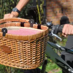 Un joli panier en osier pour vélo, doublé d'un tissu à carreaux rouges et blancs, prêt pour une promenade champêtre.