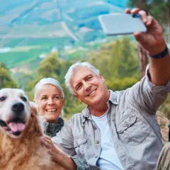 Couple prend un selfie avec leur chien lors d'une randonnée. Ils semblent heureux, profitant de la nature. Une belle journée pour faire garder son chien chez soi, loin des soucis.