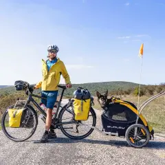Cycliste souriant avec son chien dans une remorque, prêt pour une aventure. Combien de km à vélo avec un chien ?