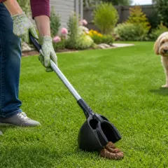 Une personne utilise une pelle pour ramasser des crottes de chien dans un jardin verdoyant. Un chien blond regarde au loin.