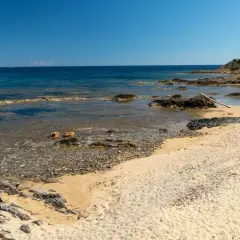Plage sauvage Narbonne, sable doré, rochers sombres et mer bleue limpide sous un ciel clair. Un coin de paradis préservé.