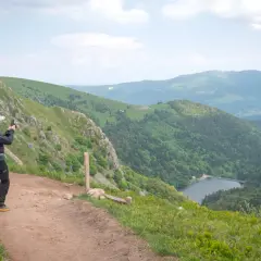 Un randonneur prend une photo du lac depuis un sentier escarpé dans les Vosges.
