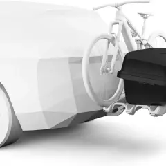 Un coffre sur attelage noir est fixé à l'arrière d'une voiture blanche stylisée, avec un vélo blanc monté juste devant.
