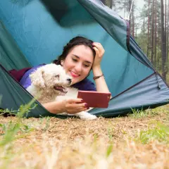 Une jeune femme et son chien profitent d'un moment de détente dans une tente, un décor parfait pour le camping acceptant les chiens.