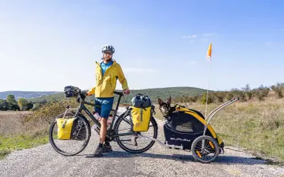 Cycliste souriant avec son chien dans une remorque, prêt pour une aventure. Combien de km à vélo avec un chien ?