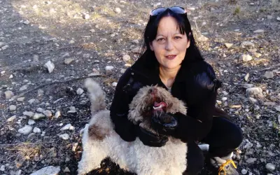 Une femme accroupie montre une truffe trouvée par son chien truffier. Le chien, un Lagotto romagnolo, tient la truffe dans sa gueule.