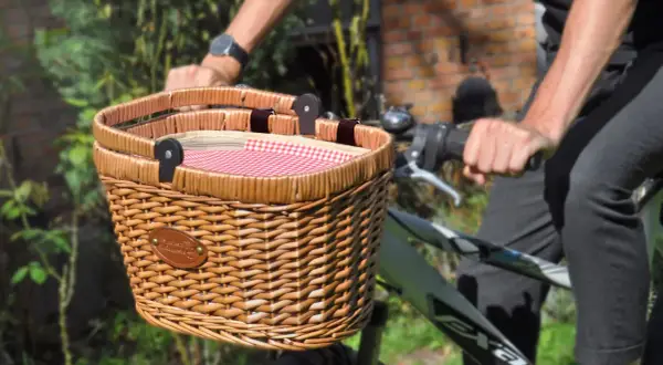 Un joli panier en osier pour vélo, doublé d'un tissu à carreaux rouges et blancs, prêt pour une promenade champêtre.