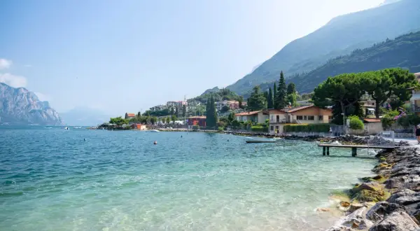 Vue paisible du lac de Garde, parfait pour la baignade. Des maisons colorées bordent la côte, adossées à des montagnes verdoyantes.