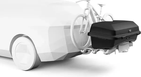 Un coffre sur attelage noir est fixé à l'arrière d'une voiture blanche stylisée, avec un vélo blanc monté juste devant.