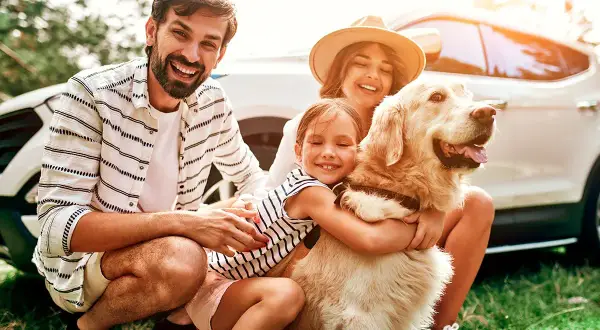 Une famille heureuse avec son chien, prête pour un week-end d'aventure. Idéal pour savoir où partir avec son chien en week-end.