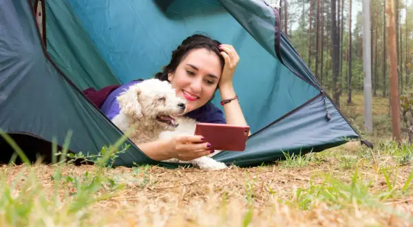 Une jeune femme et son chien profitent d'un moment de détente dans une tente, un décor parfait pour le camping acceptant les chiens.