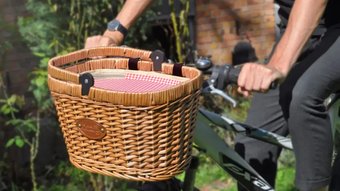 Un joli panier en osier pour vélo, doublé d'un tissu à carreaux rouges et blancs, prêt pour une promenade champêtre.