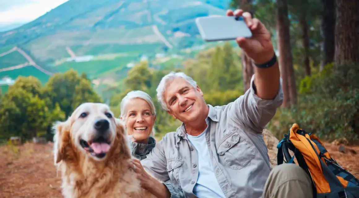 Couple prend un selfie avec leur chien lors d'une randonnée. Ils semblent heureux, profitant de la nature. Une belle journée pour faire garder son chien chez soi, loin des soucis.