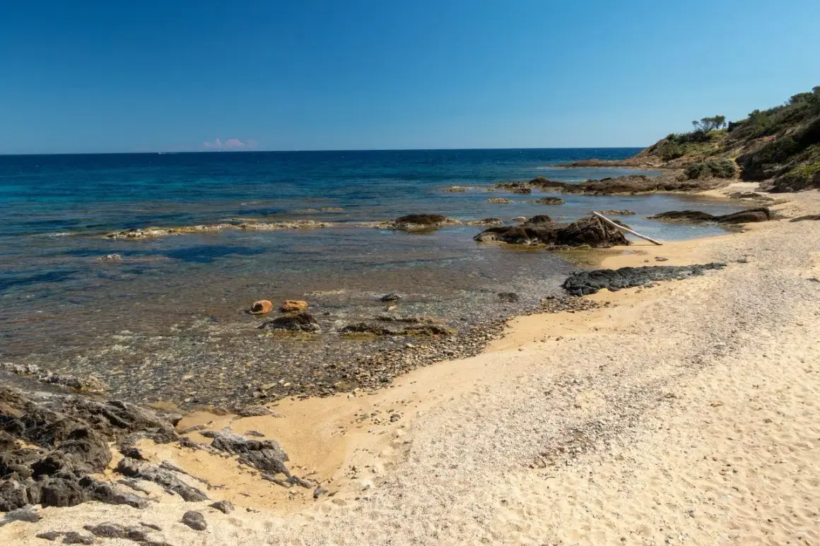 Plage sauvage Narbonne, sable doré, rochers sombres et mer bleue limpide sous un ciel clair. Un coin de paradis préservé.