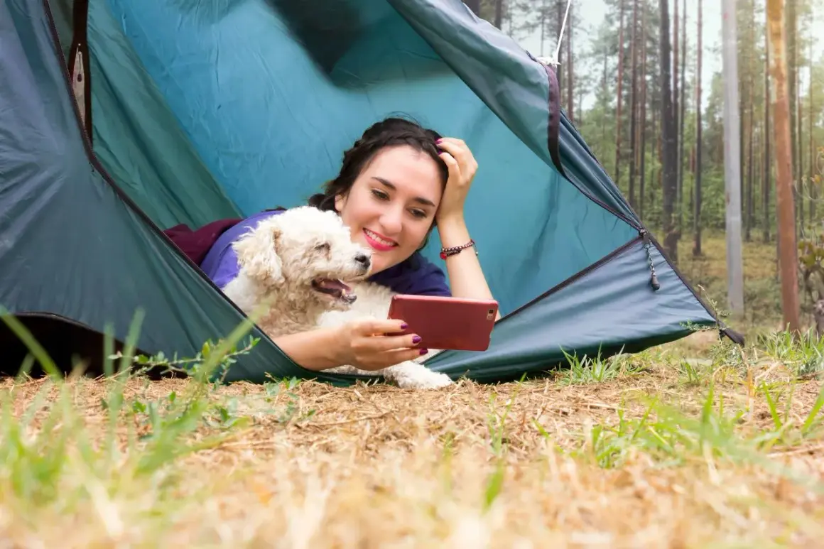 Une jeune femme et son chien profitent d'un moment de détente dans une tente, un décor parfait pour le camping acceptant les chiens.