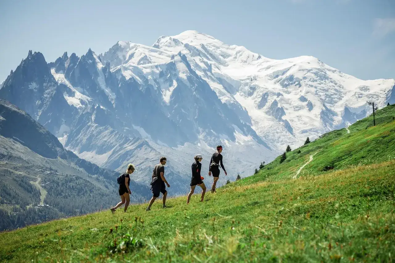 Quatre randonneurs gravissent une pente verdoyante, le Mont Blanc enneigé en toile de fond. Une belle randonnée à Chamonix.