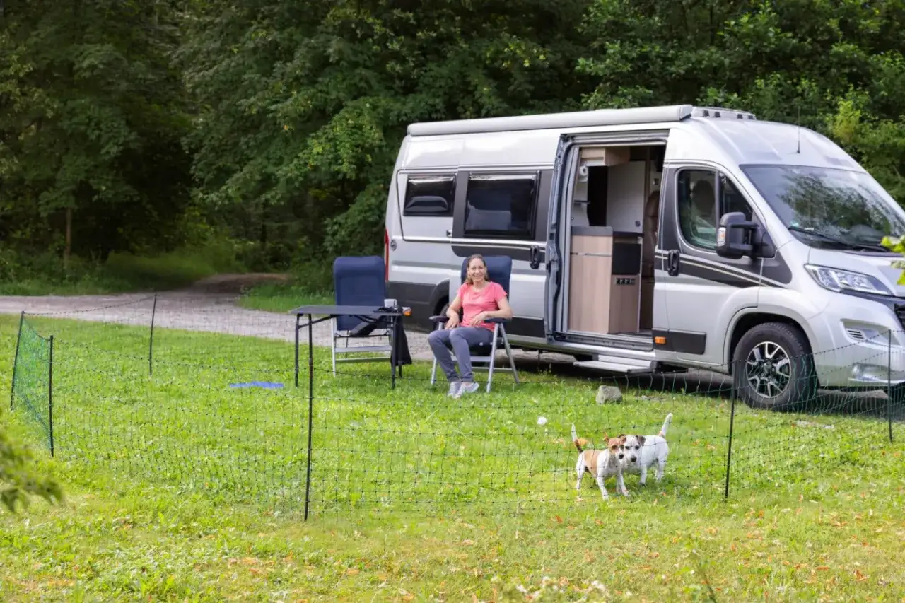 Une femme se détend près de son camping-car, tandis que ses deux chiens jouent en toute sécurité derrière une barrière chien camping-car.