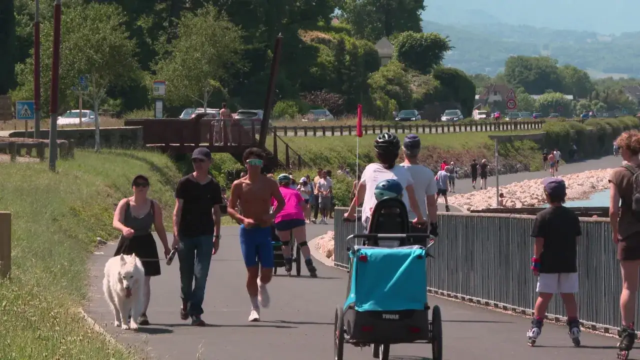 Une famille promène son chien blanc près du lac du Bourget. Des gens font du roller et du vélo sur la piste cyclable.