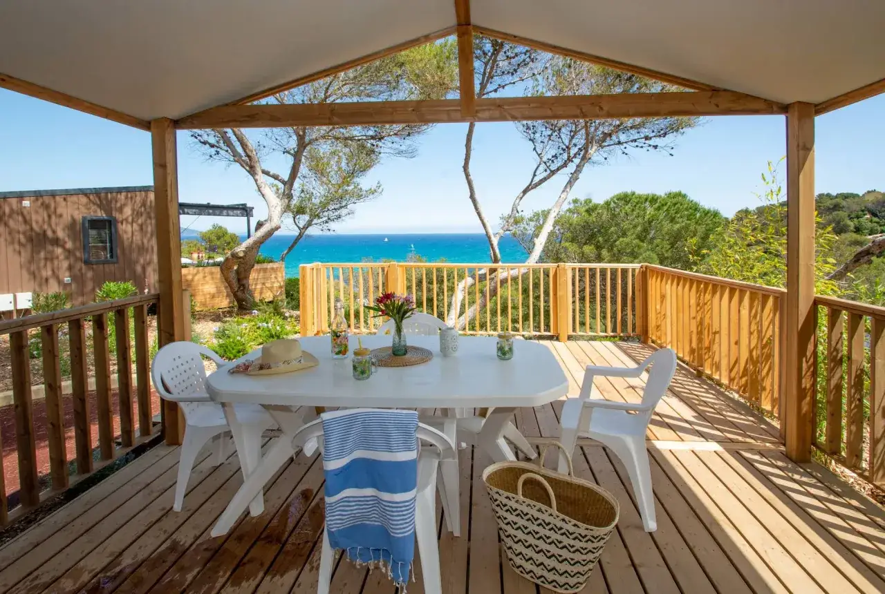 Terrasse de camping avec vue mer, table et chaises prêtes pour un repas. Idéal pour un séjour où les camping chiens acceptés sont les bienvenus.